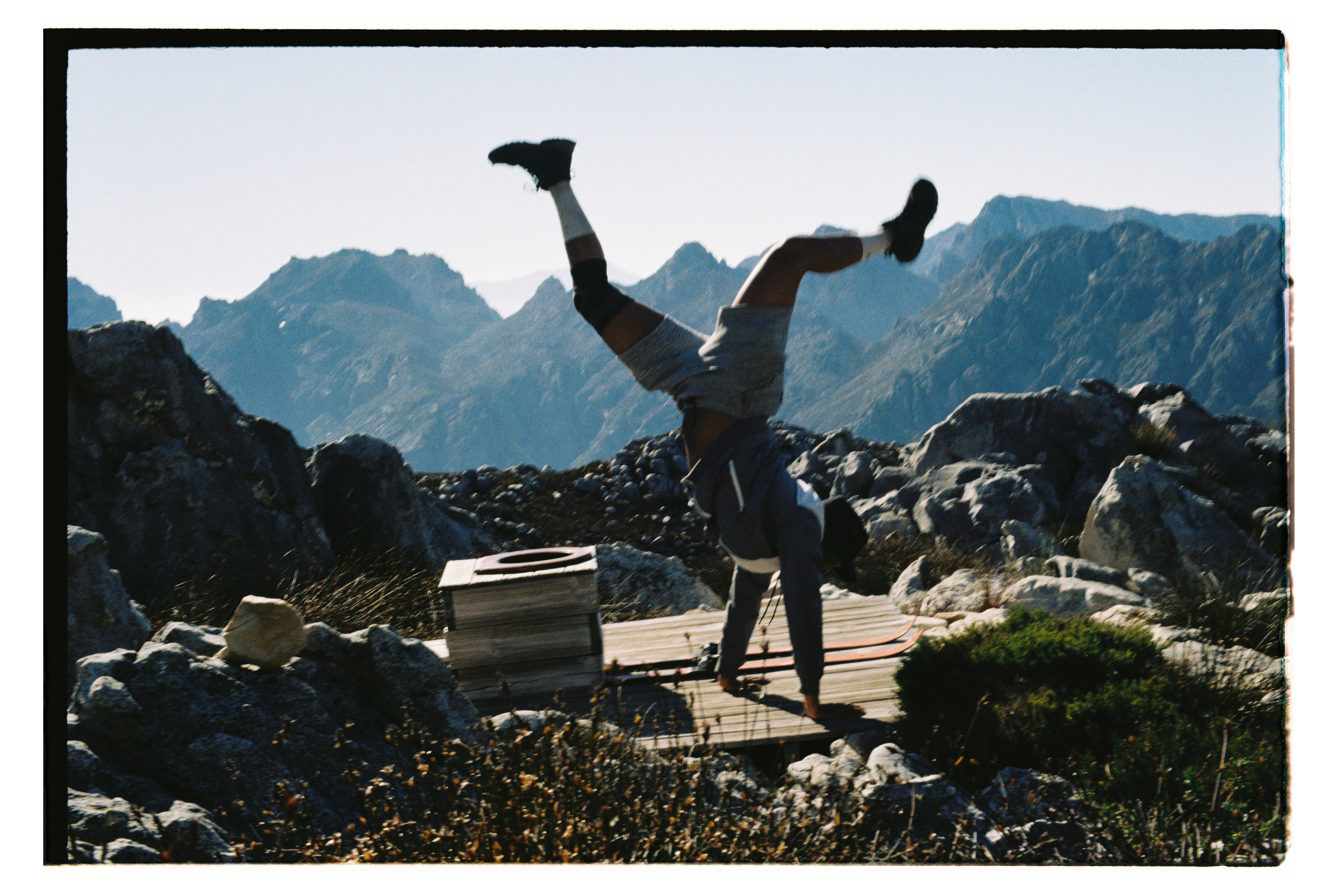 Man does handstand near a long drop toilet on a mountain.