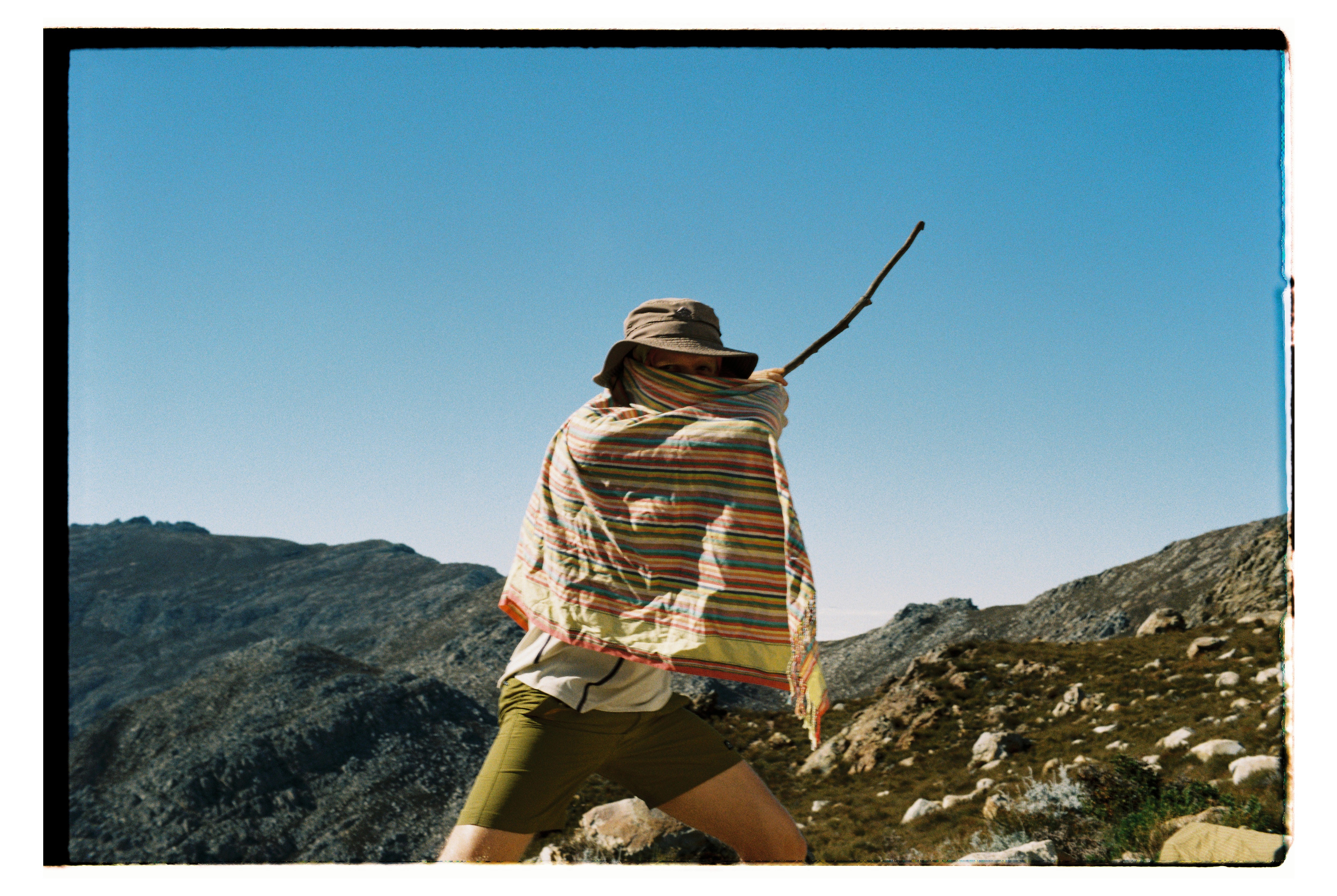 Man covered in shawl holding a stick on a mountainside
