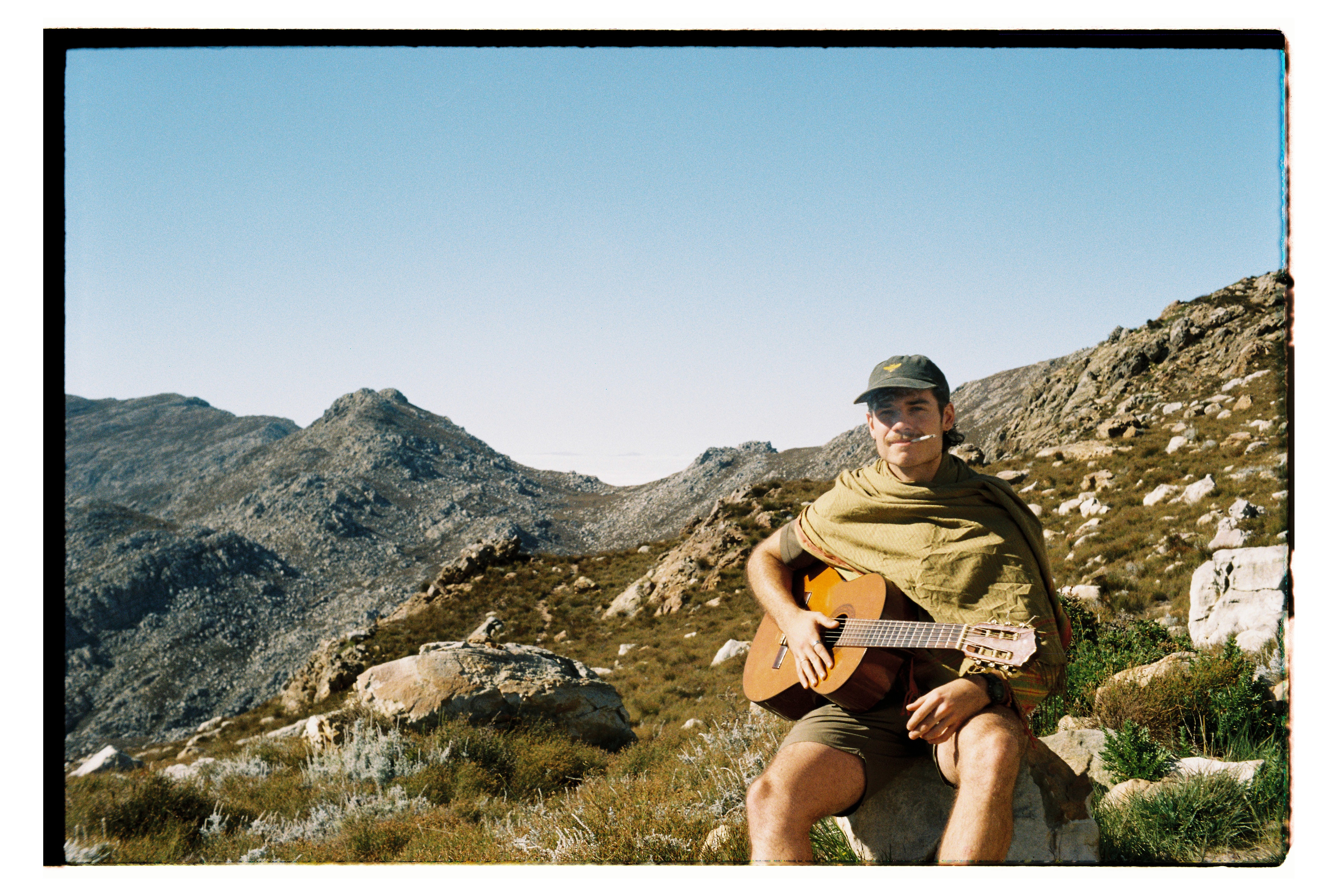 Man on a mountain smoking a cigarette with a ukulele.