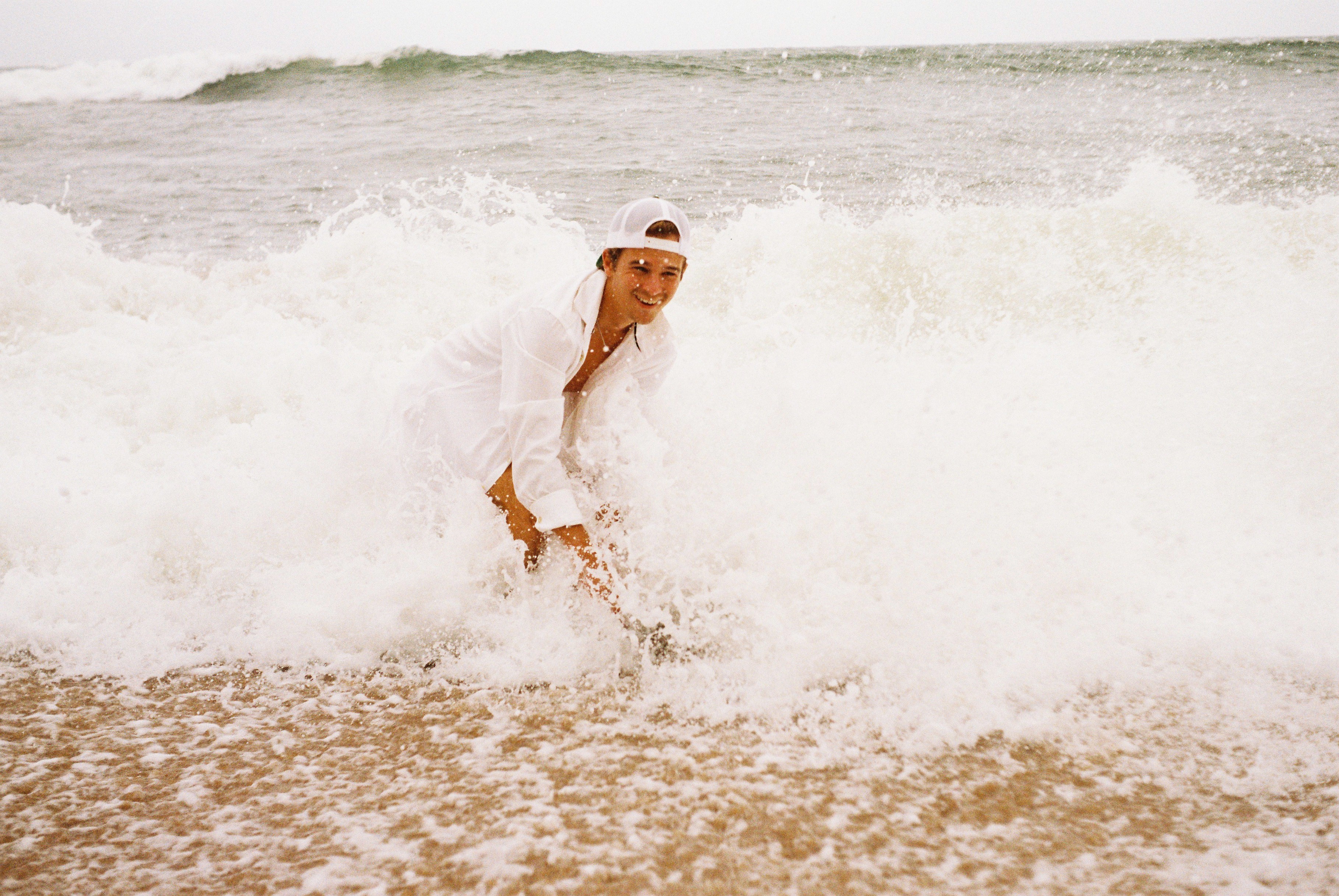 Man smiling at the beach while waves crash into him.