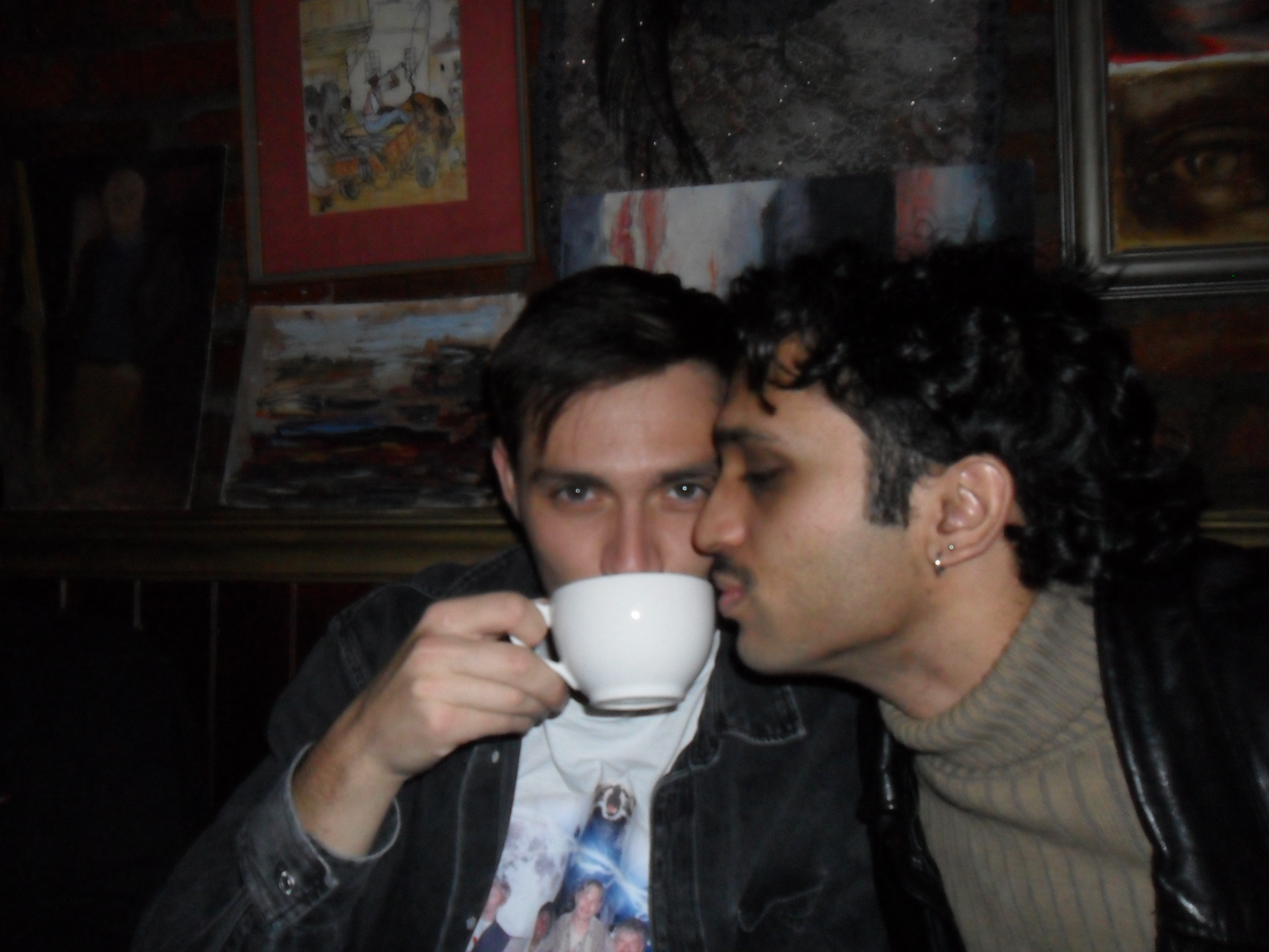 A man drinks coffee out a mug while another man also tries to drink from it.